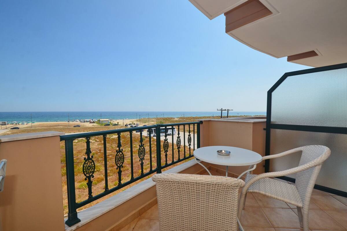 A balcony with a view of the beach, a table, and wicker chairs.