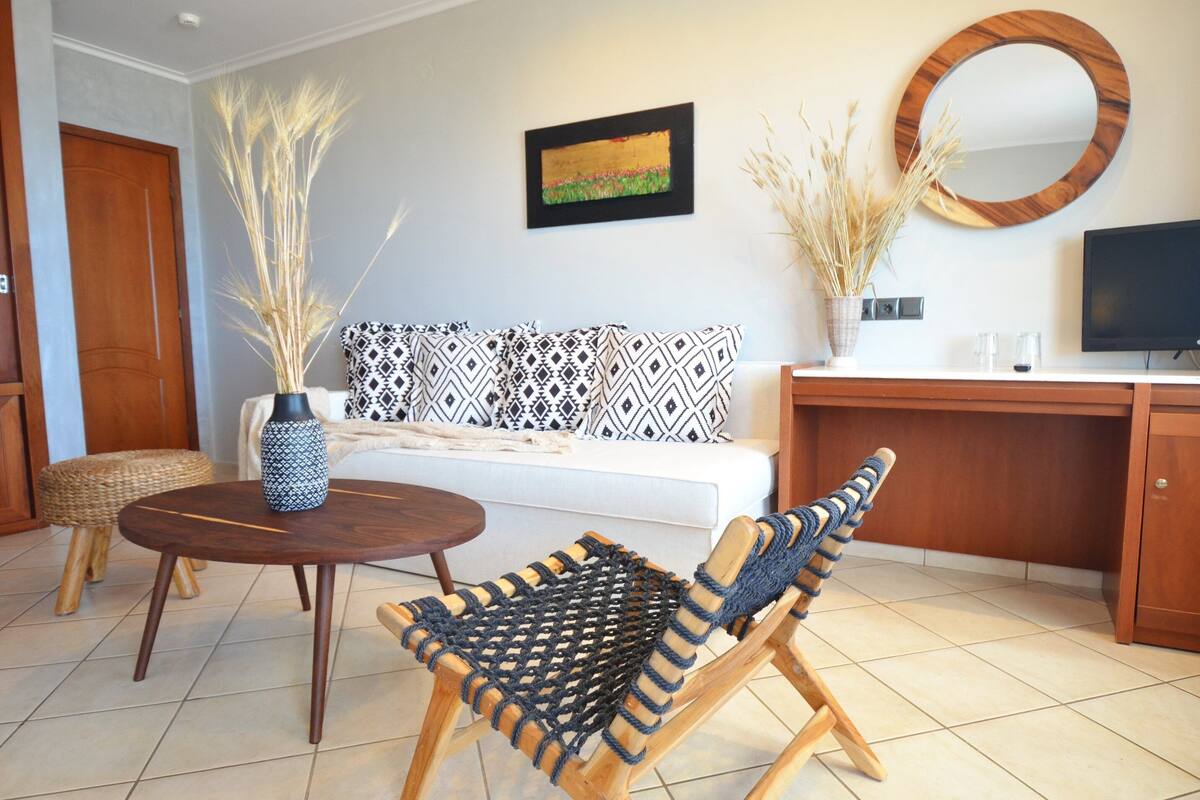A living room with a sofa, a round wooden table, a woven chair, a TV, and a mirror on the wall.