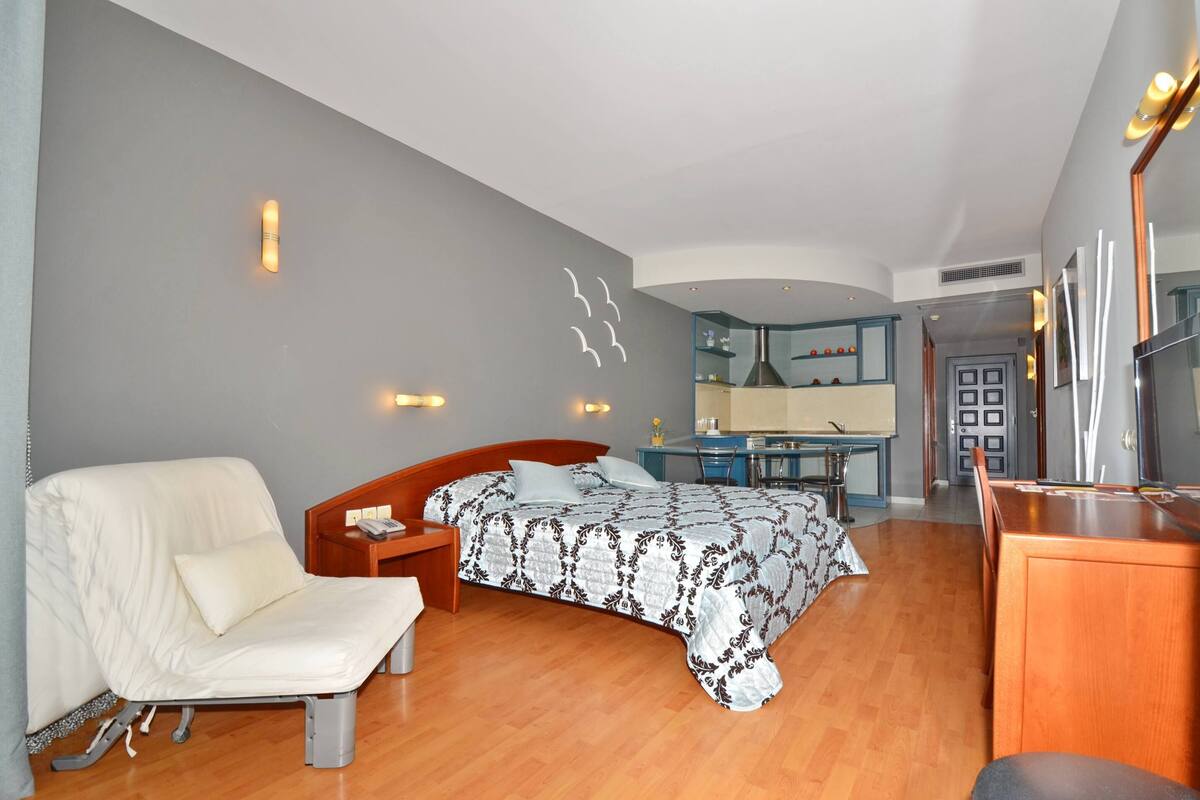 A bedroom with a bed, a chair, a desk, and a mirror.