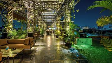 Terraço externo com estrutura metálica, plantas em vasos, áreas de estar e vista para a paisagem urbana.