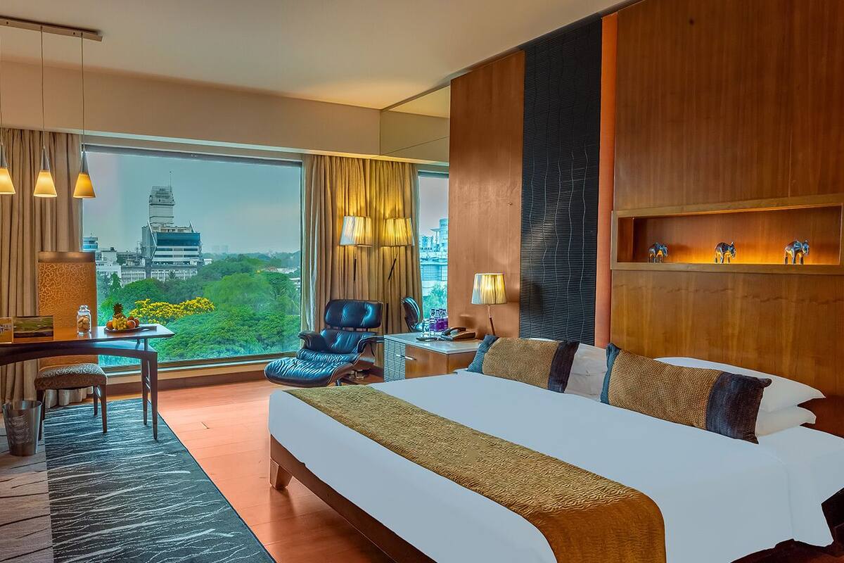 Quarto de hotel com uma cama grande, uma escrivaninha, uma cadeira e vista para a paisagem urbana.