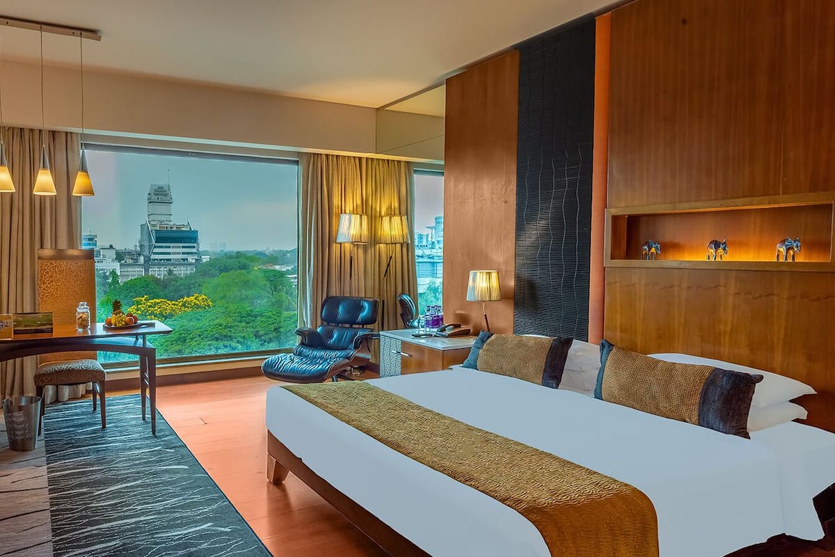 Habitación de hotel con una cama grande, un escritorio, una silla y vistas a un paisaje urbano.