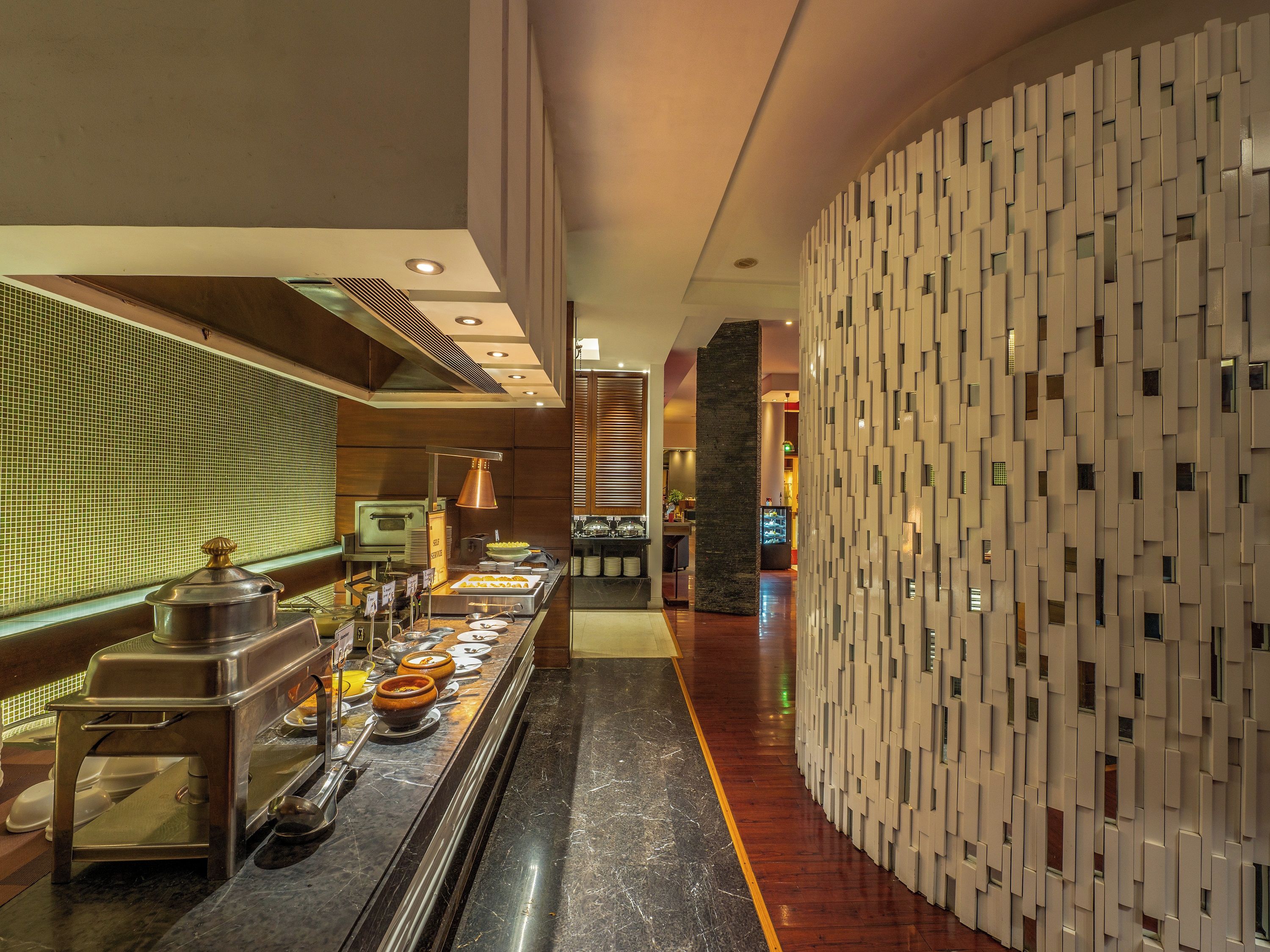 A modern hotel lobby with a buffet area featuring stainless steel appliances and a variety of food items.