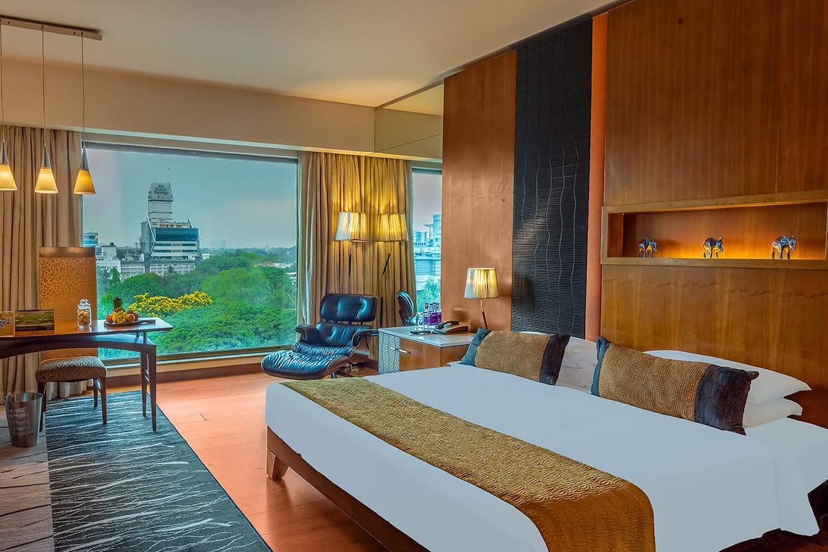 Quarto de hotel com uma cama grande, uma escrivaninha, uma cadeira e vista para a paisagem urbana.