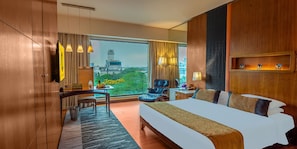 Quarto de hotel com uma cama grande, uma escrivaninha, uma cadeira e vista para a paisagem urbana.