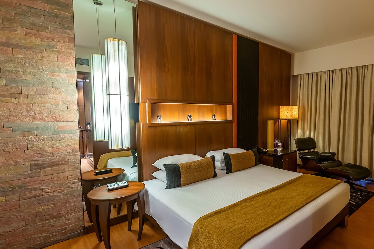 Quarto de hotel com uma cama grande, uma escrivaninha, uma cadeira, uma televisão e um espelho.