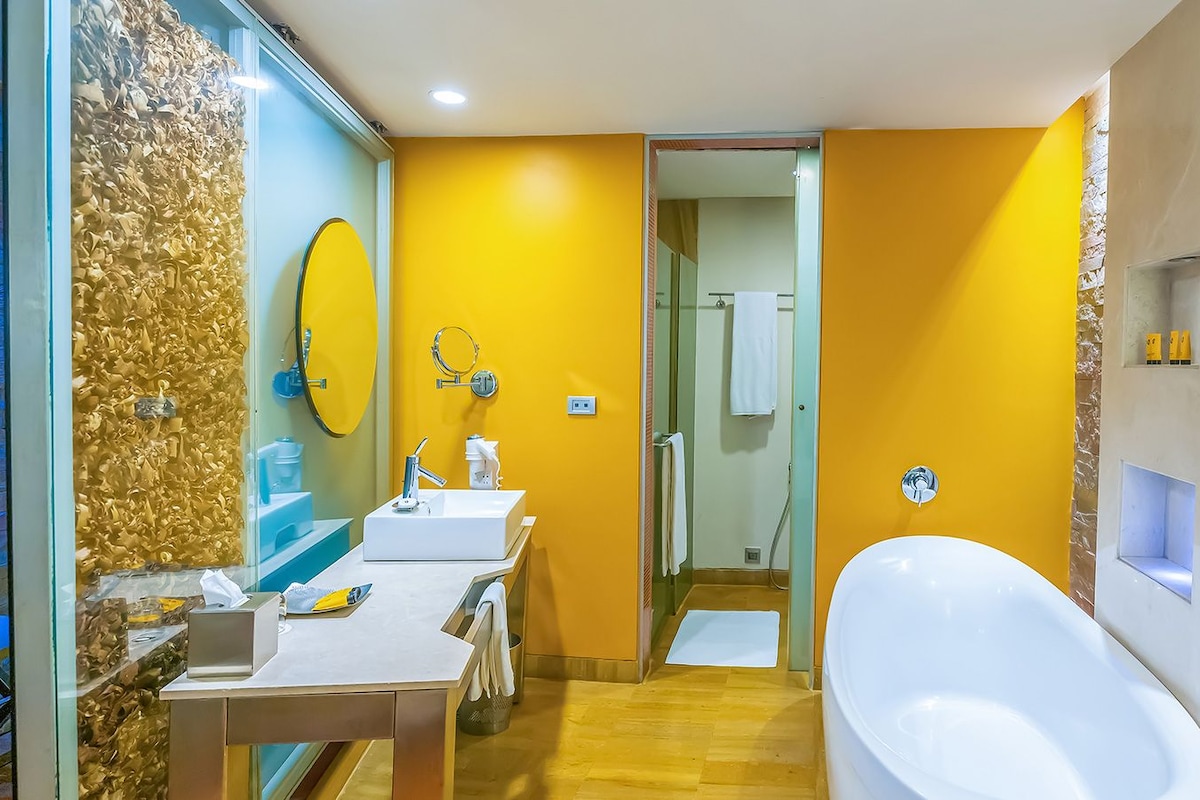 Un bagno moderno con una parete gialla a contrasto, una vasca da bagno ampia e un mobile lavabo con specchio e lavandino.