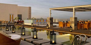 Uma área de piscina no terraço com espreguiçadeiras, mesas e lanternas.