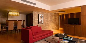 A modern living room with a red sofa, a dining area with chairs, a stone accent wall, and a television. - The O Hotel (Pune)