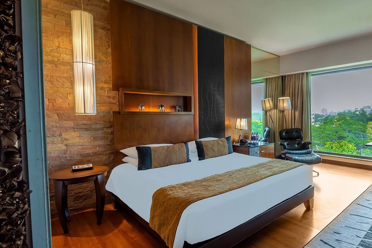 Quarto de hotel moderno com uma cama grande, escrivaninha, cadeira e vista para a cidade.