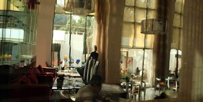 A dining area with a glass partition, a table with chairs, and a view of the outside. - The O Hotel (Pune)