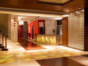 Um saguão de hotel com balcão de recepção, escada e parede decorativa.