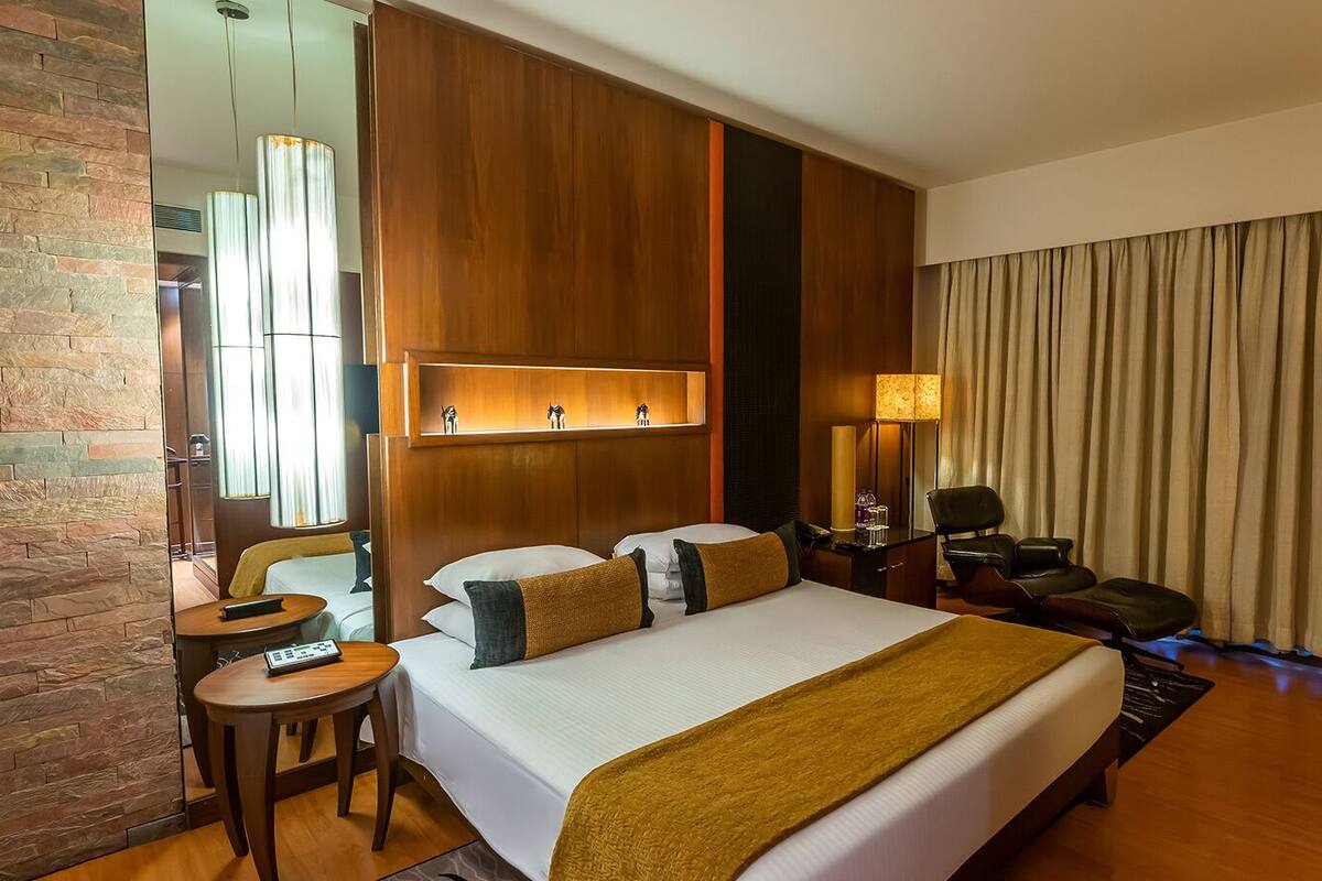 Quarto de hotel com uma cama grande, uma escrivaninha, uma cadeira, uma televisão e um espelho.
