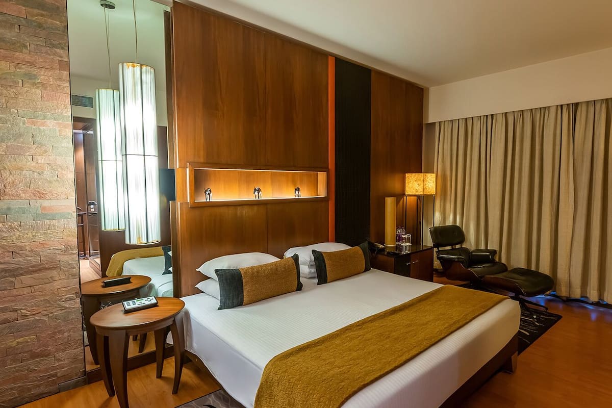 Habitación de hotel con una cama grande, un escritorio, una silla, un televisor y un espejo.