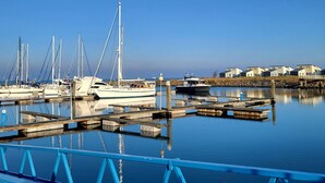 Ein Yachthafen mit vertäuten Booten, ruhigem Wasser und einer Gebäudereihe im Hintergrund.
