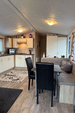 Een compacte woonruimte met een kitchenette, een eethoek met stoelen, een bank en een klein vloerkleed.