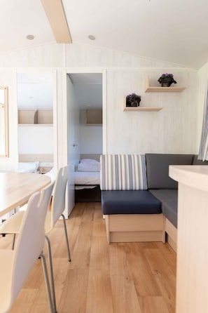 Ein gemütlicher Raum mit einem Bett, einer Sitzecke mit Kissen, einem Tisch mit Stühlen und integrierten Regalen mit Dekoration.