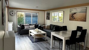 A modern living room with a sofa, a dining table with chairs, a coffee table, and a clock on the wall. - RBR 1654 - Beach Resort Kamperland by Interhome (Kamperland)