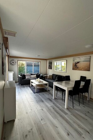A modern living room with a sofa, a dining table with chairs, a coffee table, and a clock on the wall. - RBR 1654 - Beach Resort Kamperland by Interhome (Kamperland)