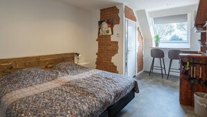 Een slaapkamer met een bed, een bureau, twee stoelen, een raam en een bakstenen muur.