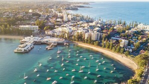 An aerial view of a coastal city with a marina, buildings, and clear blue waters. - KozyGuru | Manly | Prime Manly Coastal Hub (Manly)