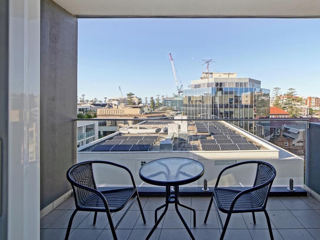 A balcony with two chairs and a table, overlooking a cityscape with buildings and solar panels.