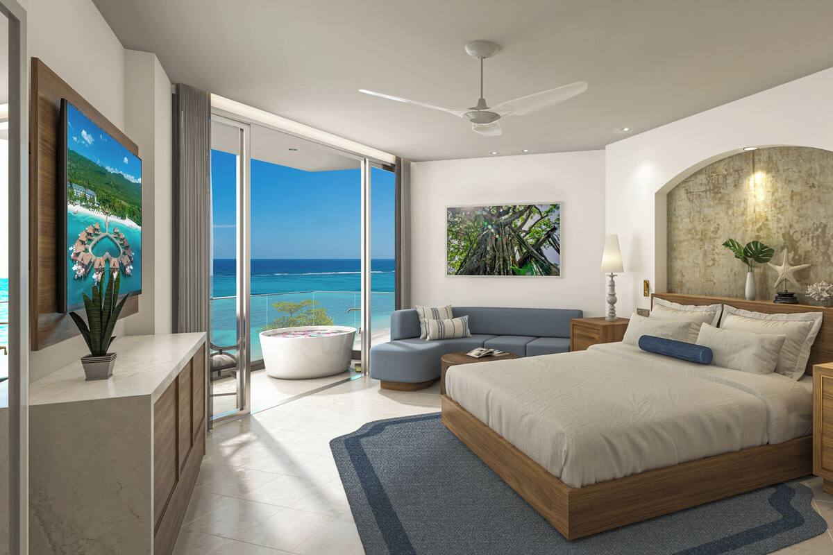 Un dormitorio moderno con una cama grande, un sofá, un escritorio y vistas al océano.