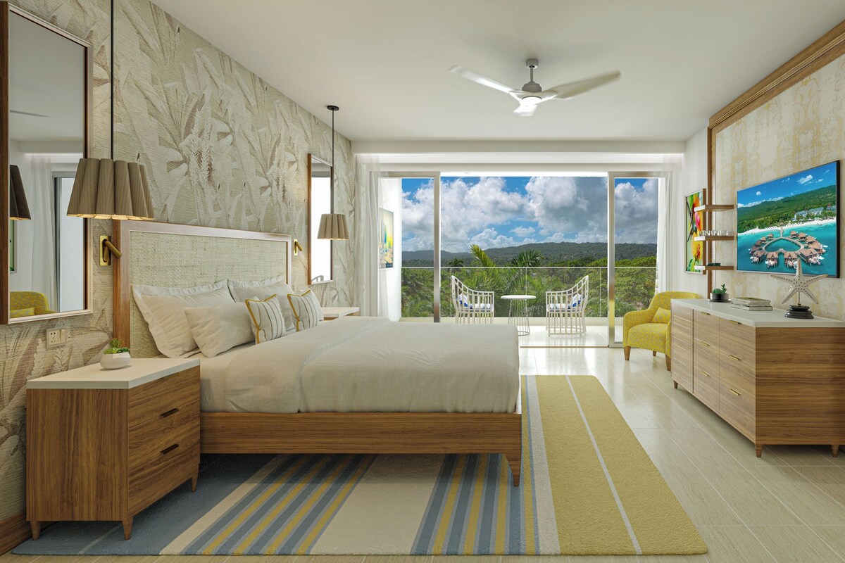 A bedroom with a large bed, a TV, a balcony with a view, and a bathroom with a vanity.