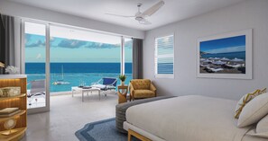 A hotel room with a large bed, a desk, a chair, a small table with a plant, and a view of the ocean. - Sandals Dunn's River Falls (Ocho Rios)