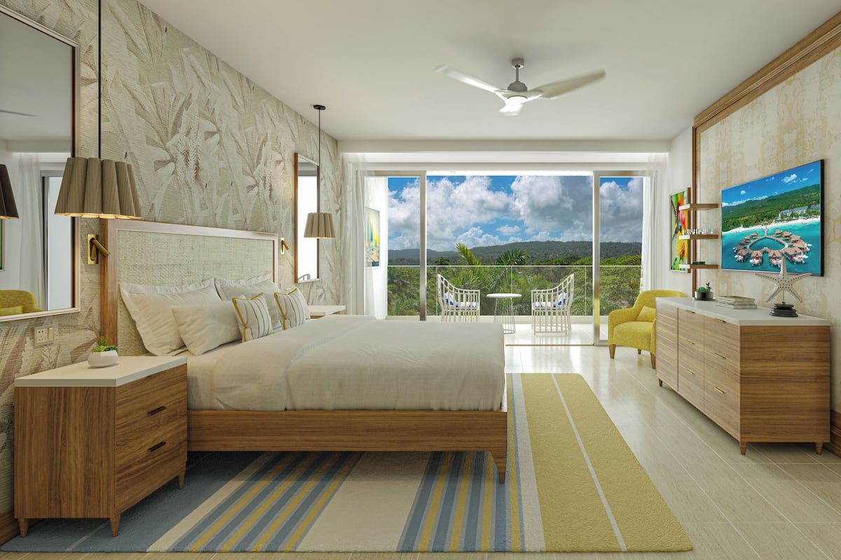 Un dormitorio con una cama grande, televisor, balcón con vistas y baño con tocador.