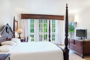 A spacious bedroom with a large bed, a television, and a view of greenery through the windows.