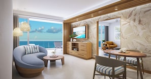A modern living room with a curved sofa, a round coffee table, and a dining area with a wooden table and chairs. A television is mounted on the wall, and there is a view of the sea through large windows.
