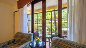 A room with two striped sofas, a small round table with a vase of flowers, and a large window with a view of greenery.
