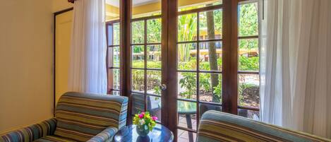 A room with two striped sofas, a small round table with a vase of flowers, and a large window with a view of greenery.