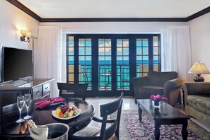 A hotel room with a balcony, a dining table with fruit and glasses, a sofa, a TV, and a lamp. - Sandals Dunn's River Falls (Ocho Rios)