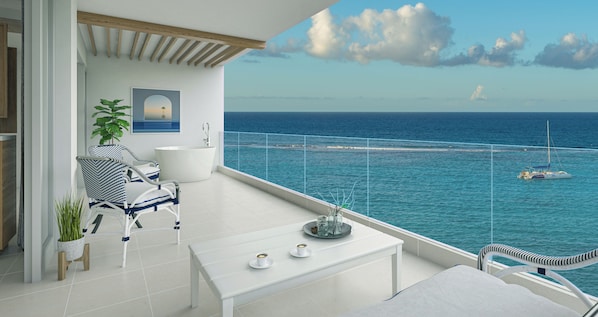 A balcony with a view of the sea, a white bathtub, and a seating area with chairs and a table.