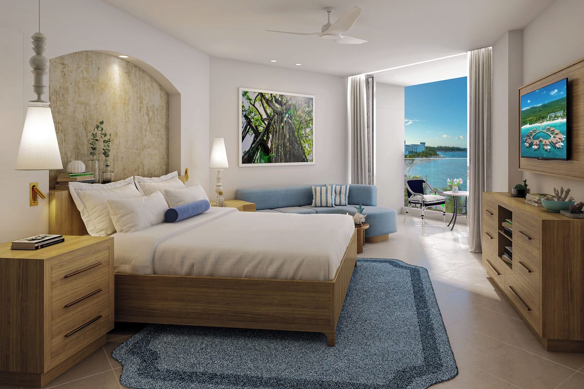 Una habitación de hotel moderna con una cama, un televisor, un balcón con vistas al mar y un escritorio con una lámpara.