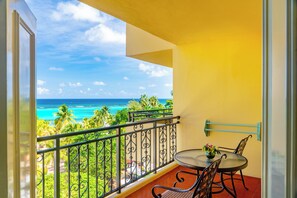 A balcony with a view of the ocean, a table with chairs, and a railing. - Sandals Dunn's River Falls (Ocho Rios)