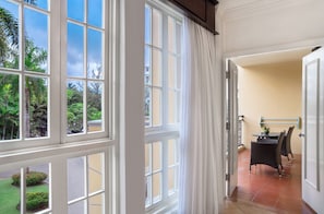 A room with large windows, a dining area with a table and chairs, and a view of greenery outside.