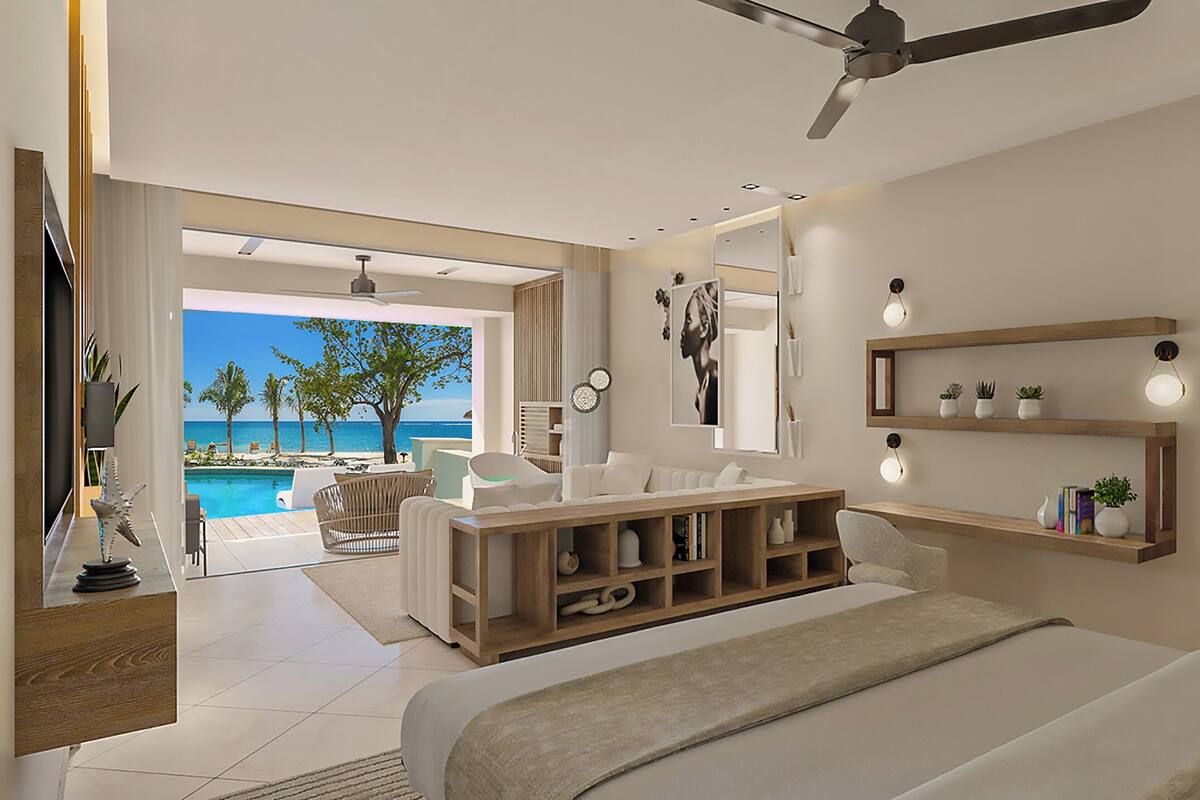 Un dormitorio moderno con una cama grande, un ventilador de techo, una mesita de noche de madera, una mesilla con lámpara, un espejo amplio y vistas a una piscina y una playa.