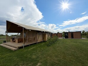 Ein Campingplatz mit einem großen Zeltbereich, einer Holzterrasse und einem kleinen Gebäude.