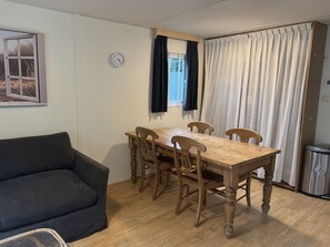 Ein Essbereich mit einem Holztisch und Stühlen, einer Uhr an der Wand und einem Fenster mit Vorhängen.