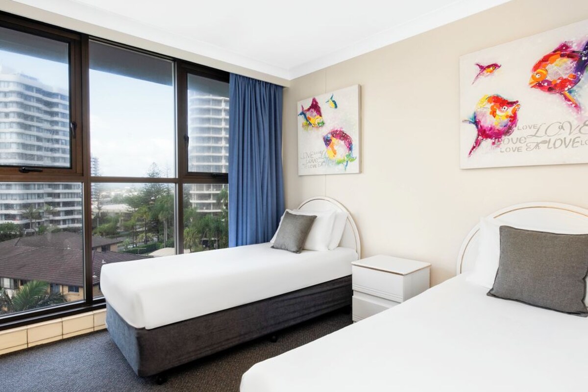Habitación de hotel con dos camas, un ventanal con vistas a edificios y una obra de arte en la pared.
