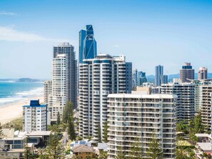 Un paysage urbain côtier avec de hauts immeubles, dont un gratte-ciel remarquable avec une façade en verre bleue, et une plage en arrière-plan.
