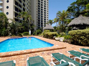 A swimming pool with lounge chairs, palm trees, and a tall building in the background. - Breakfree Acapulco Surfers Paradise (Gold Coast)