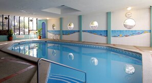 Una piscina interior amb paret de rajola amb un disseny de ones, un rellotge i una planta en test.