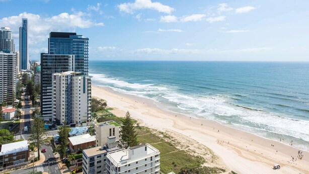 A coastal cityscape with high-rise buildings, a beach, and a clear sky.