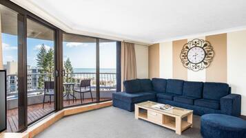 Una sala de estar moderna con un ventanal grande, un sofá azul, una mesa de centro de madera y un reloj decorativo en la pared.