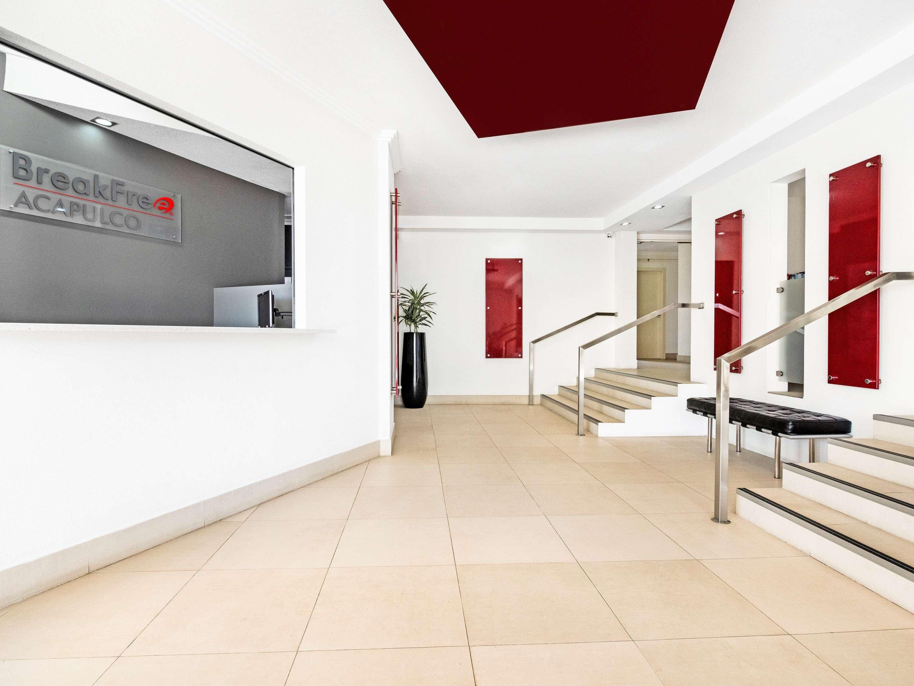 A modern reception area with a reception desk, a staircase, and red accents on the walls.
