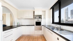 Una cocina moderna con armarios blancos, encimera negra, horno empotrado y ventana con vista a la ciudad.